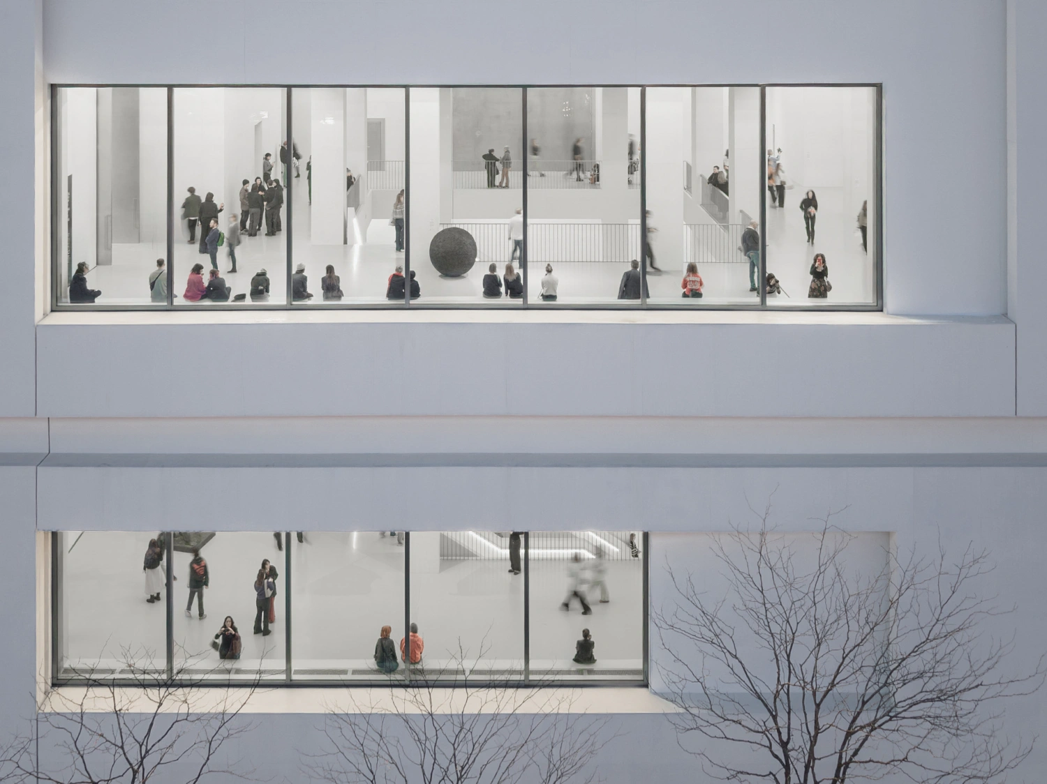 Museum of Modern Art in Warsaw by Thomas Phifer — Floor-to-ceiling glazing reveals the stacked interior volumes of Warsaw's Museum of Modern Art, with visitors distributed across multiple white concrete levels.