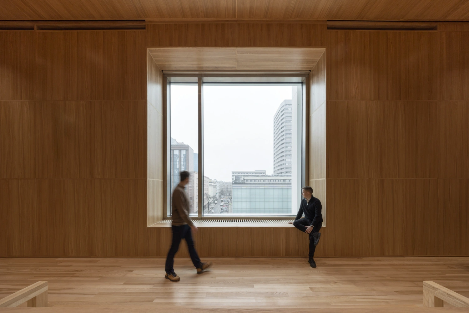 Museum of Modern Art in Warsaw by Thomas Phifer — A wood-clad interior volume frames a horizontal window opening onto Warsaw's dense urban skyline.