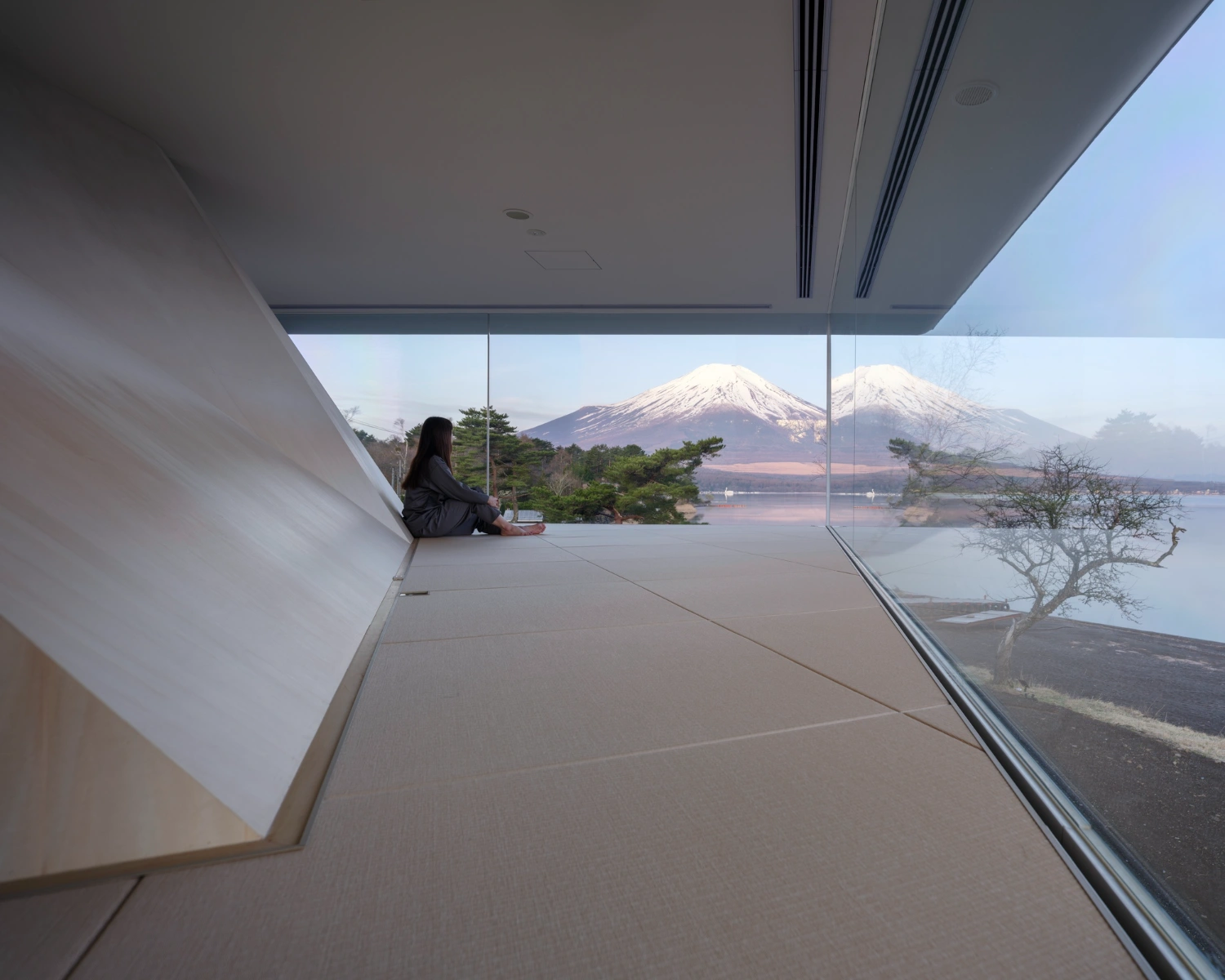 CYCL by YŪ Momoeda Architects — A single occupant sits at the threshold of CYCL's expansive glazed interior, positioned against the floor-to-ceiling frameless glass plane that frames Mount...