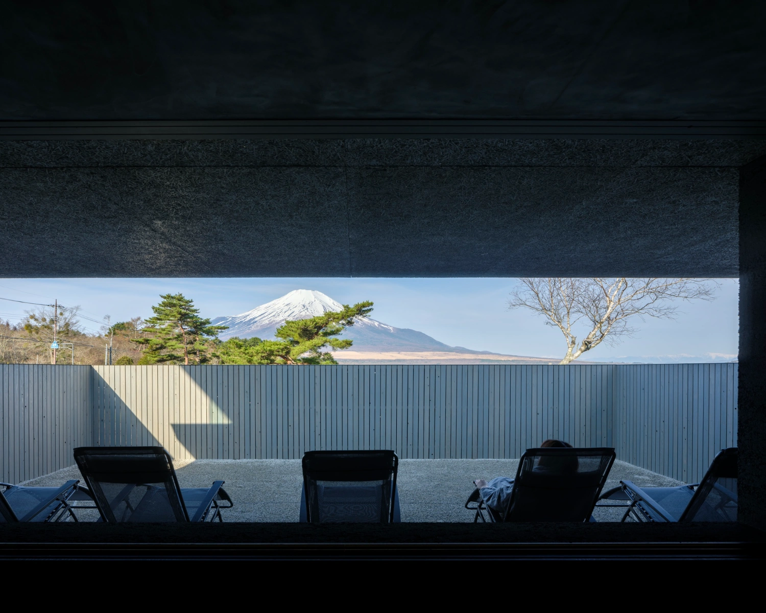 CYCL by YŪ Momoeda Architects — Interior view from a sauna facility framing Mount Fuji across a gravel courtyard.