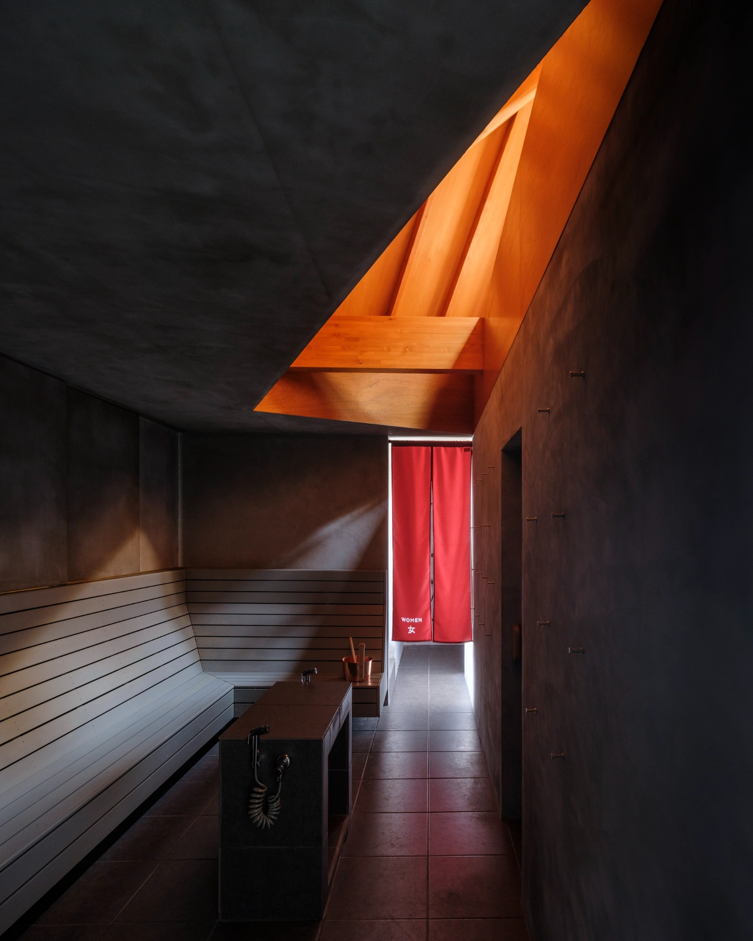 CYCL by YŪ Momoeda Architects — A sauna interior framed by a pitched timber ceiling that funnels light through a clerestory opening, casting an orange glow across white horizontal wood...