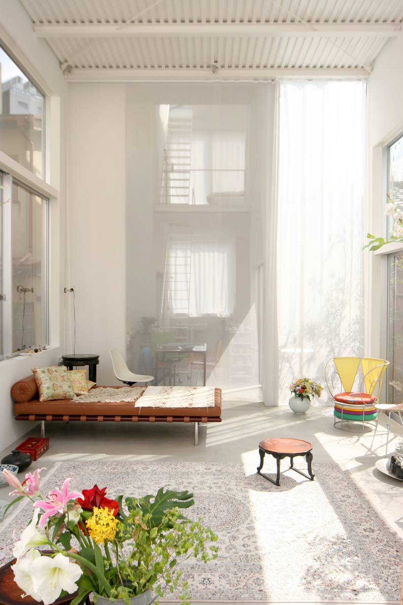 House A by Ryue Nishizawa — A sunlit interior passage frames a wooden-frame daybed with terracotta cushioning and patterned textile, positioned against the left wall.
