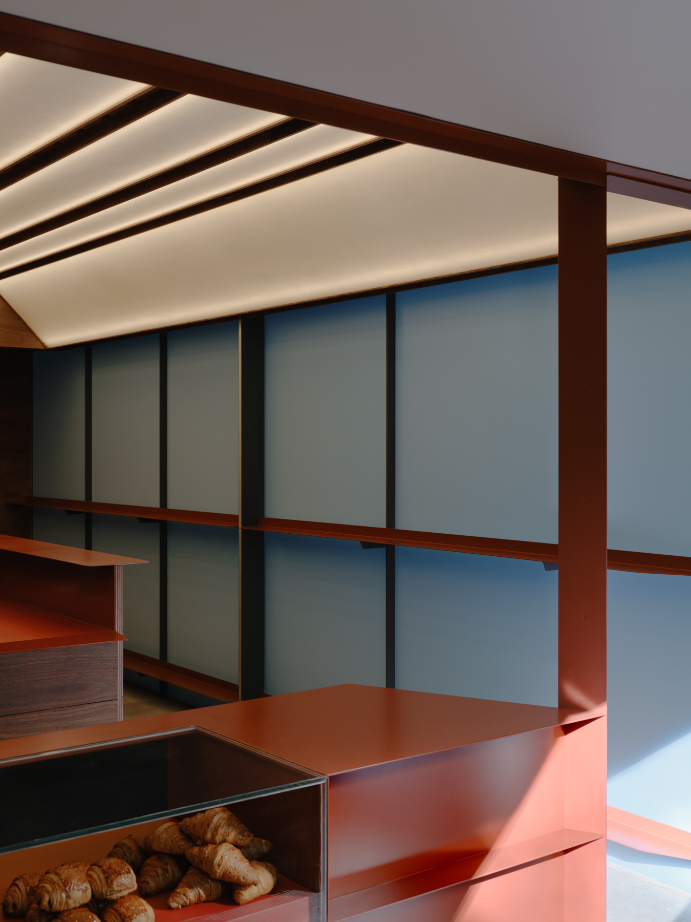 Palace Coffee by KKAP — Interior view from Palace Coffee reveals a recessed threshold where dark timber cabinetry and counter surfaces sit beneath a dramatic concrete soffit with...