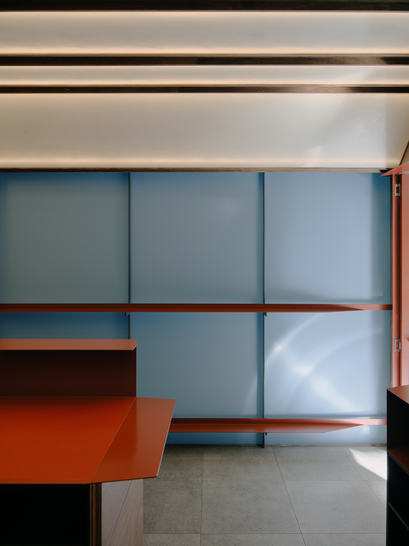 Palace Coffee by KKAP — The storefront interior is framed through seamless glazing, revealing a dark timber counter and cabinetry set against a blue-grey wall paneling.