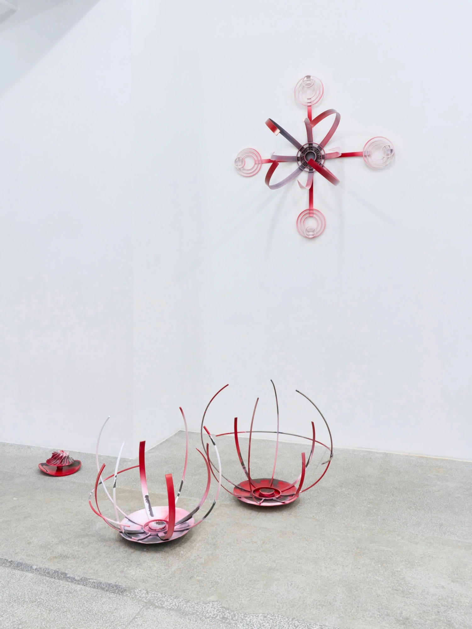 Swarm / Rój by Zuza Golinska at Piktogram — Golinska's wall-mounted sculpture presents a radial composition of pink-red wire forming nested circular elements with ribbon-like curved extensions...