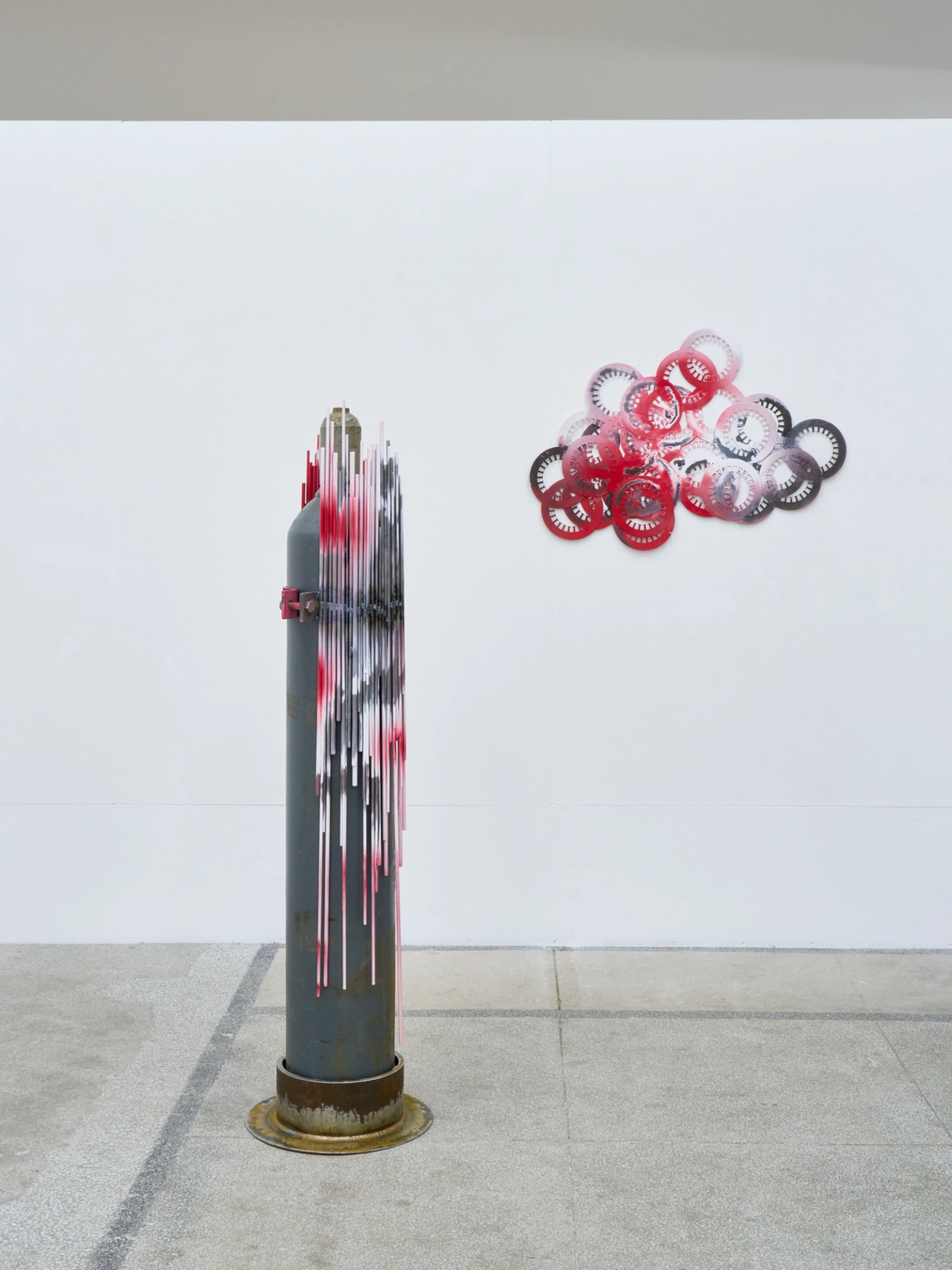 Swarm / Rój by Zuza Golinska at Piktogram — Golinska's installation pairs a vertical steel cylinder with perforated circular apertures and coiled red electrical cable against a pristine white gallery...