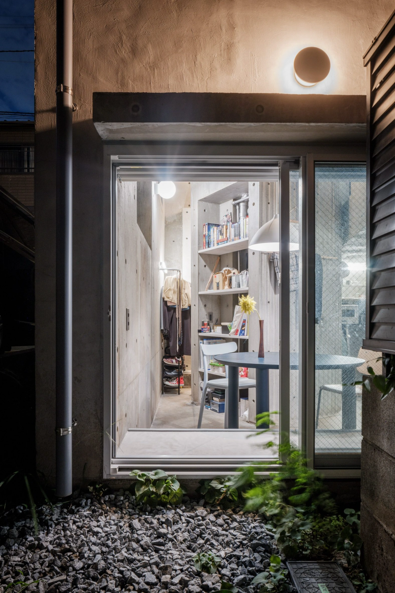 Nakano House by Suzuko Yamada Architects — Evening view through full-height glazing reveals the internal spatial organization of Nakano House's 24-square-meter footprint.