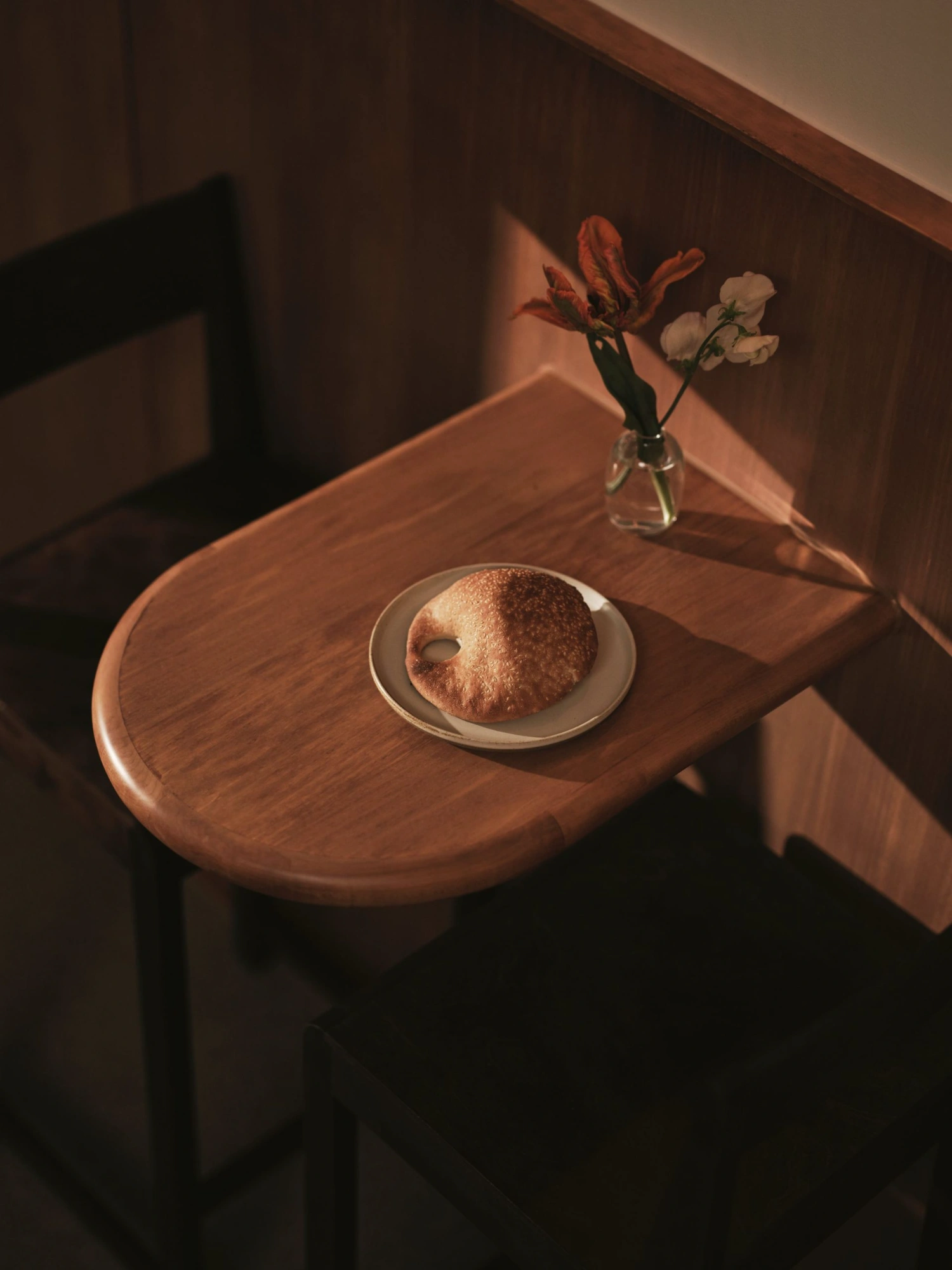 Common Breads bakery by MA Studio — A small circular timber table catches golden-hour sunlight streaming diagonally across caramel-toned wood paneling.