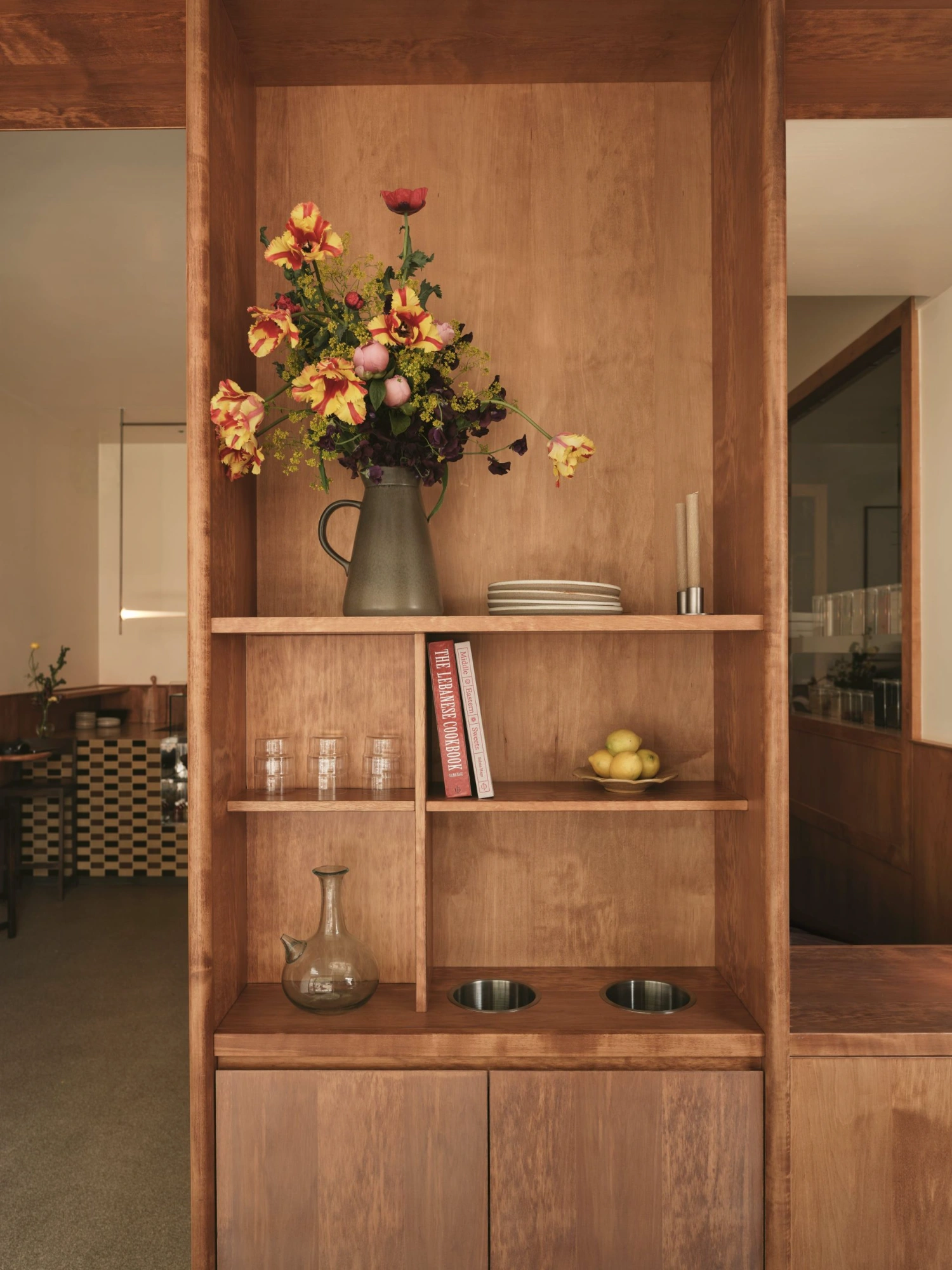 Common Breads bakery by MA Studio — Built-in timber cabinetry with walnut-toned vertical grain paneling frames a curated vase arrangement.