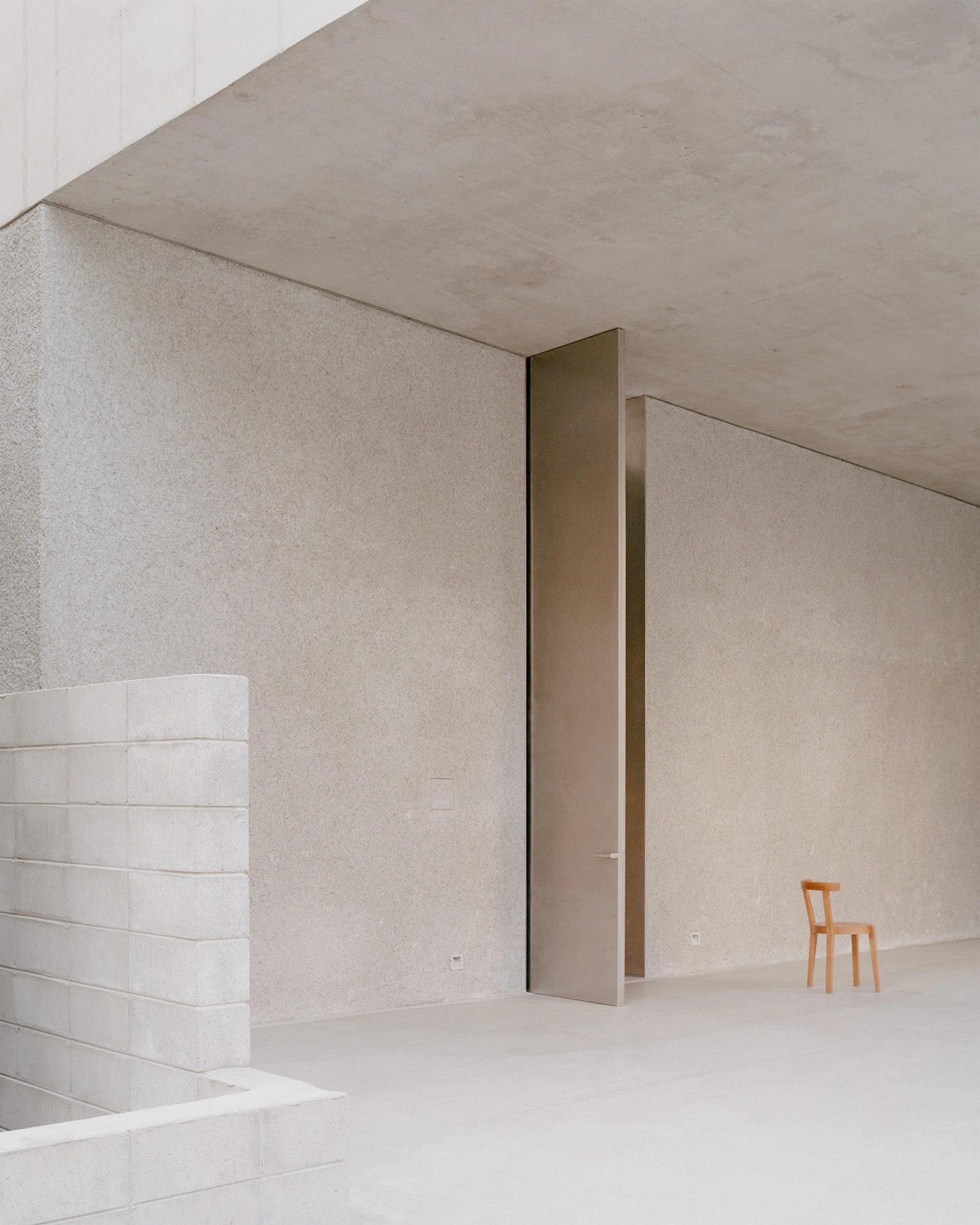 K-Auction Exhibition Hall Sinsa by min_workshop + 3ab — A double-height gallery passage anchored by a tall bronze-framed doorway that establishes sharp vertical geometry against soft-textured plaster walls in...