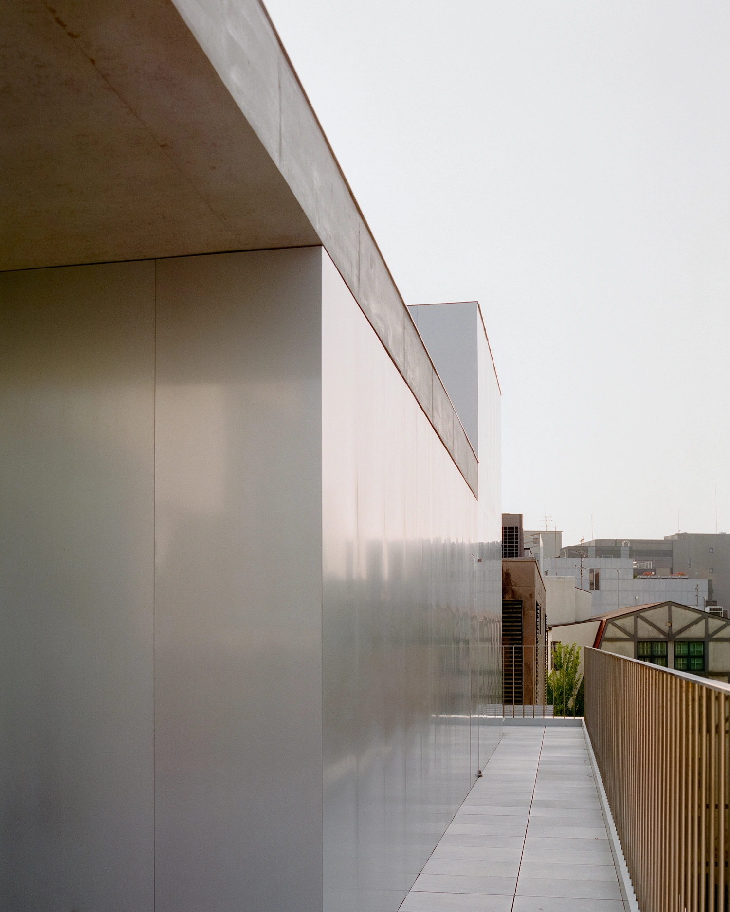 K-Auction Exhibition Hall Sinsa by min_workshop + 3ab — A rooftop passage at K-Auction Exhibition Hall features a narrow bronze-framed glass panel casting geometric shadows across a polished concrete floor.