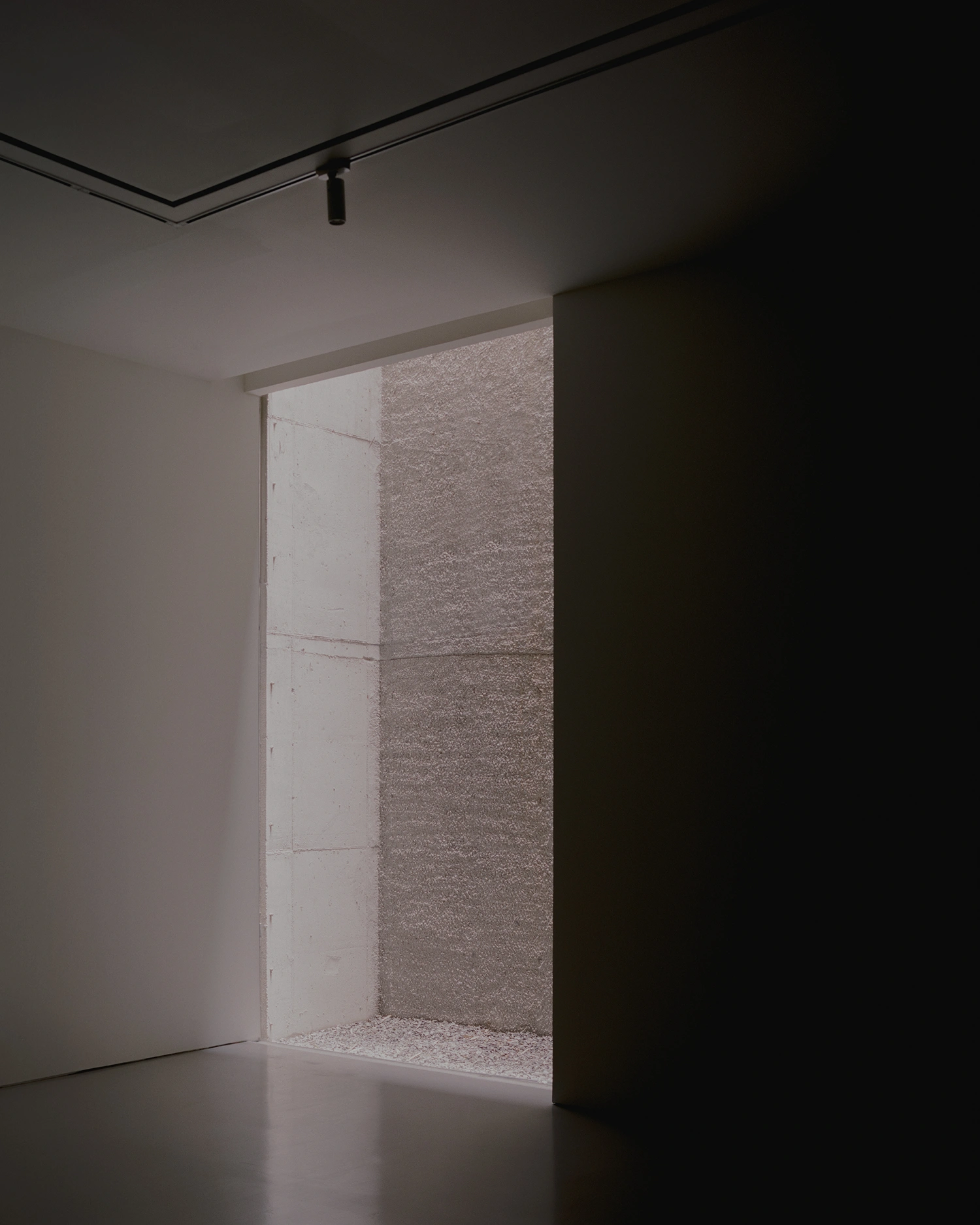 K-Auction Exhibition Hall Sinsa by min_workshop + 3ab — A narrow threshold framed by bronze-edged panels opens onto a recessed alcove lined with textured plaster.