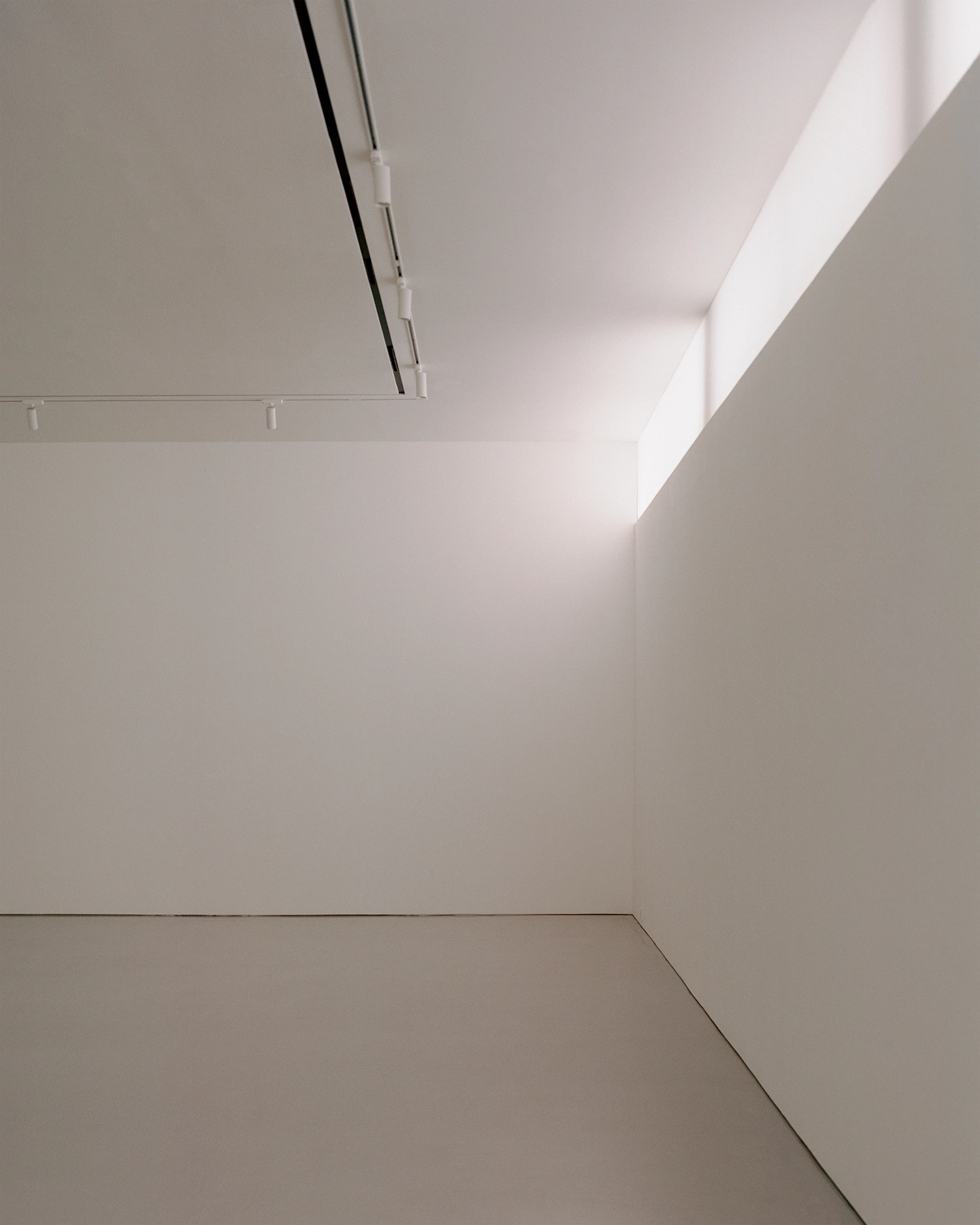 K-Auction Exhibition Hall Sinsa by min_workshop + 3ab — A vertical passage framed by austere geometries: a tall bronze-edged doorway punctuates the left wall, its dark frame providing structural emphasis against...