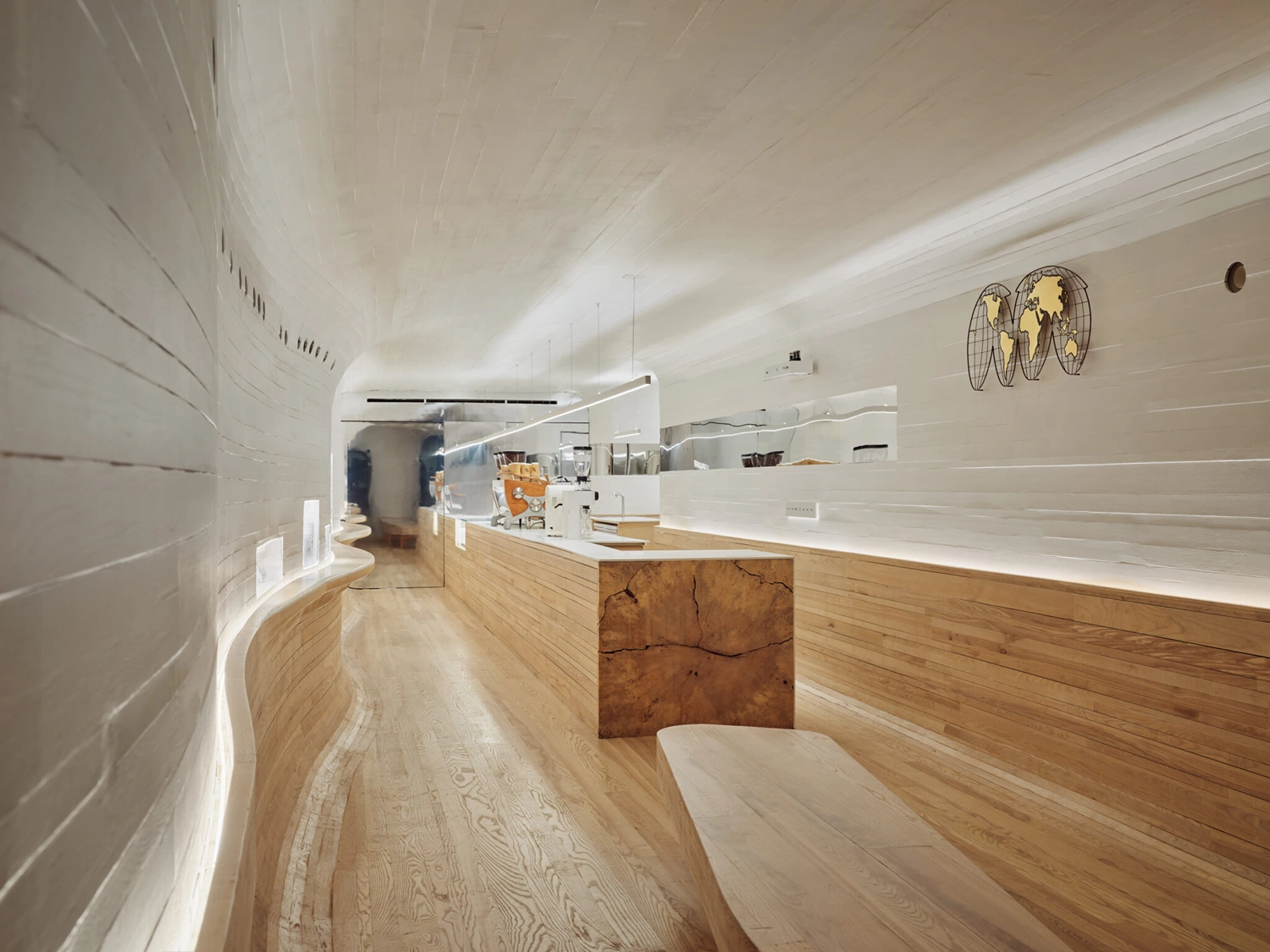 % Arabica New York Midtown by Curtis Su Associates — A subterranean coffee shop interior defined by continuous curved white-painted timber walls that flow seamlessly into an arched ceiling, creating an...