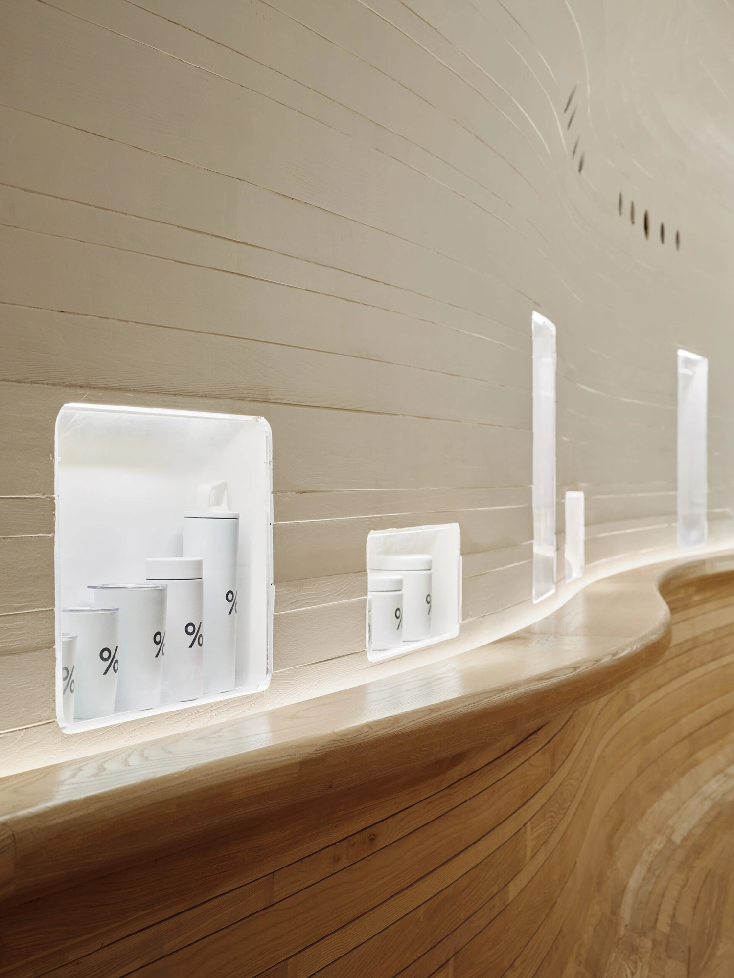 % Arabica New York Midtown by Curtis Su Associates — White-painted timber product displays line a curved wall, their cylindrical forms echoing the architecture's organic geometry.