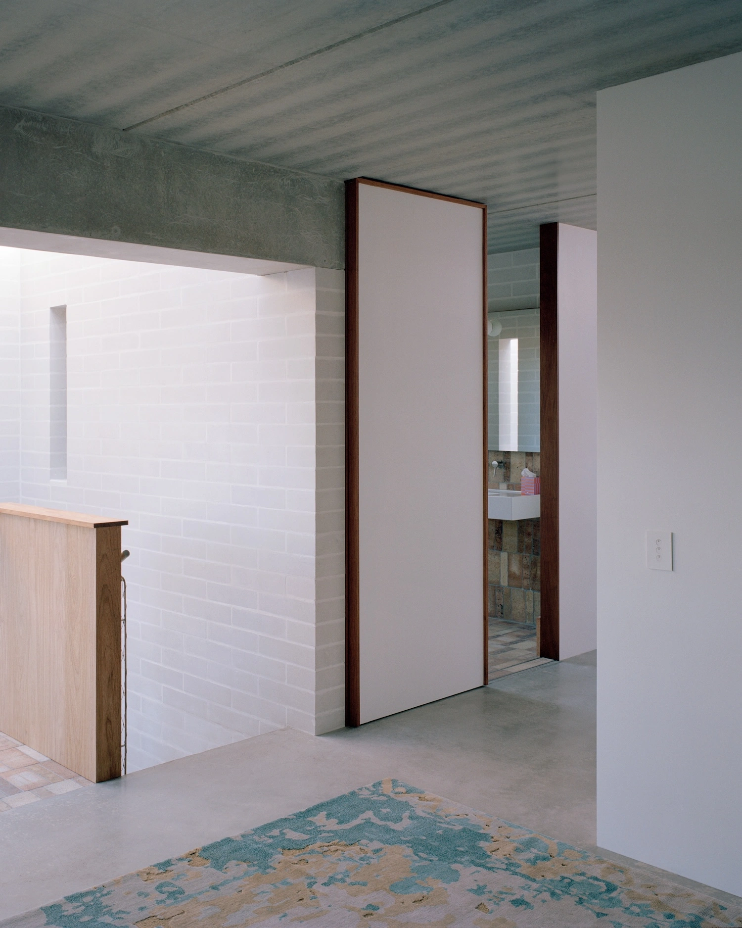 Birdwood House by Peter Besley — A bathroom threshold framed by monolithic white brick walls and dark-stained timber reveals.