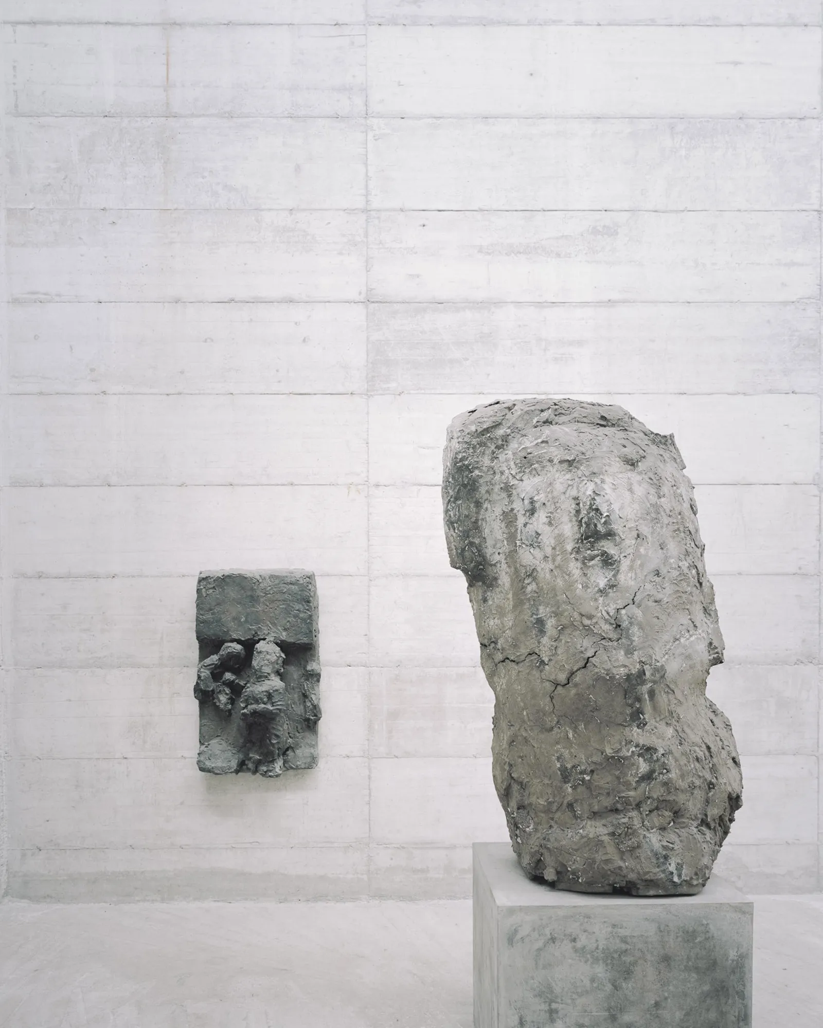 La Congiunta Museum by Peter Märkli — A narrow concrete corridor gallery within La Congiunta Museum displays two sculptural heads by Hans Josephsohn mounted on grey concrete plinths.