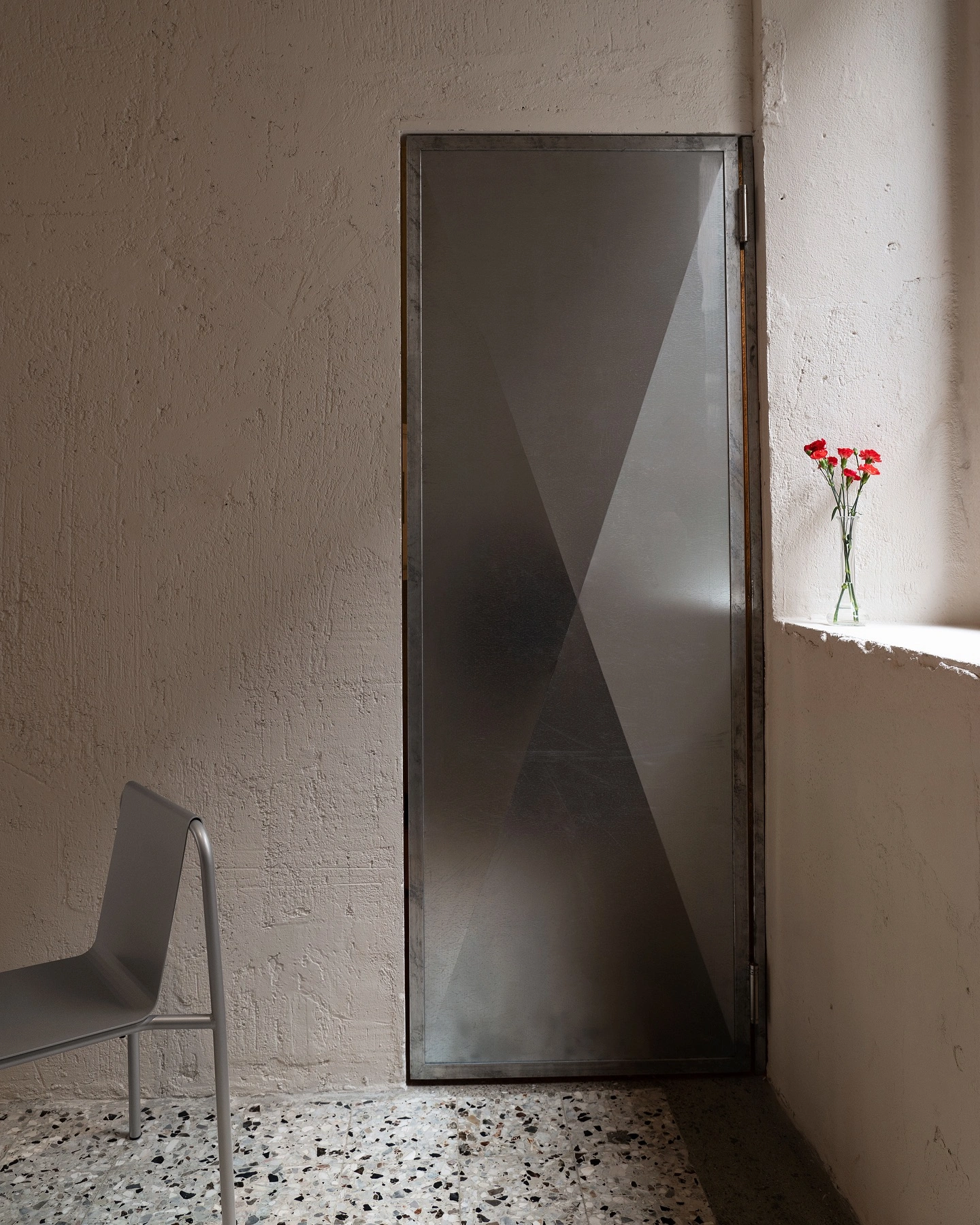 L’ALTRO by Sagoma Studio — A narrow corridor within L'ALTRO frames a tall, frosted-glass partition with dark metal frame dividing interior spaces.