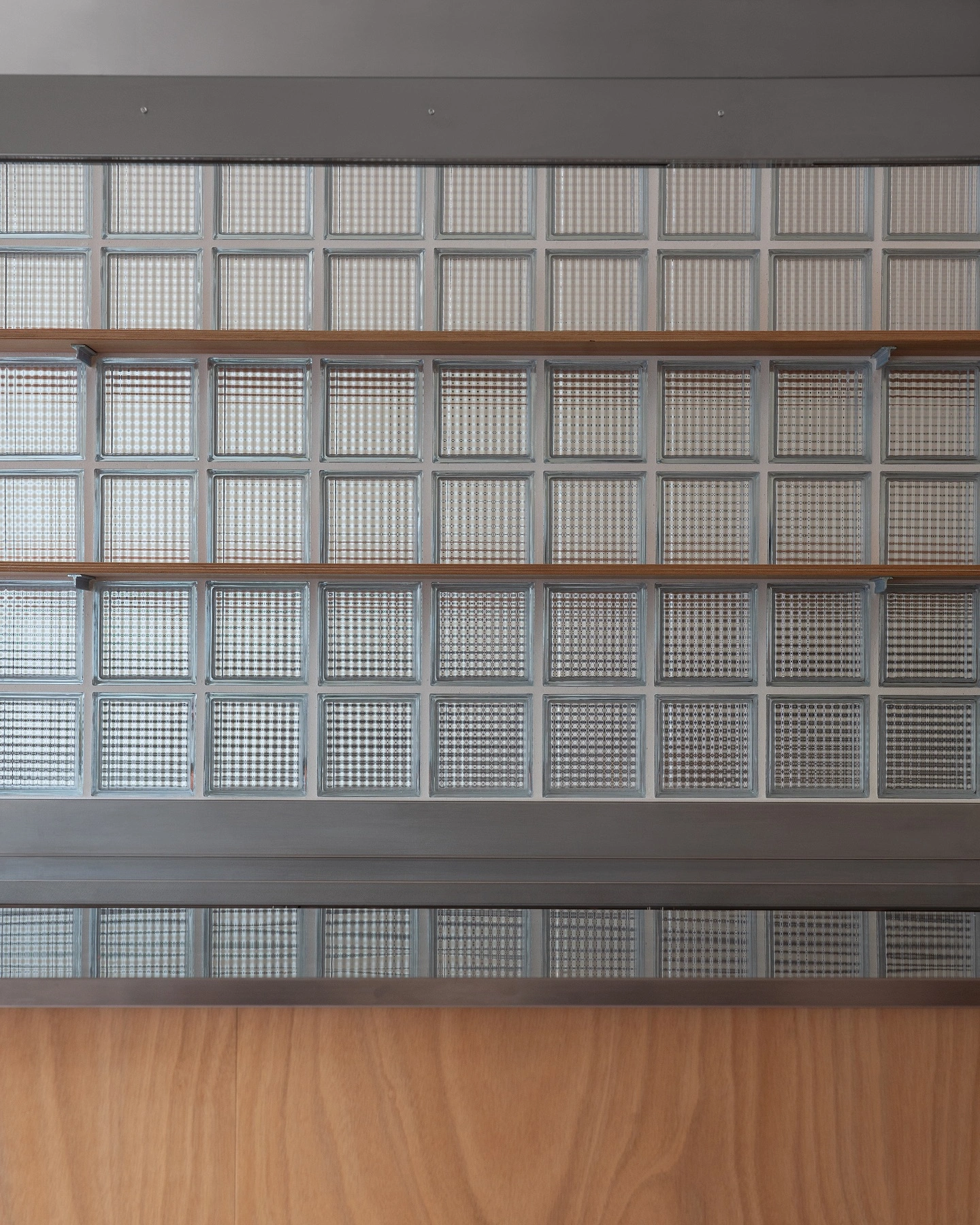L’ALTRO by Sagoma Studio — A gridded wall of translucent glass-block panels arranged in nine columns and six rows, each cell containing a fine geometric pattern that filters and...