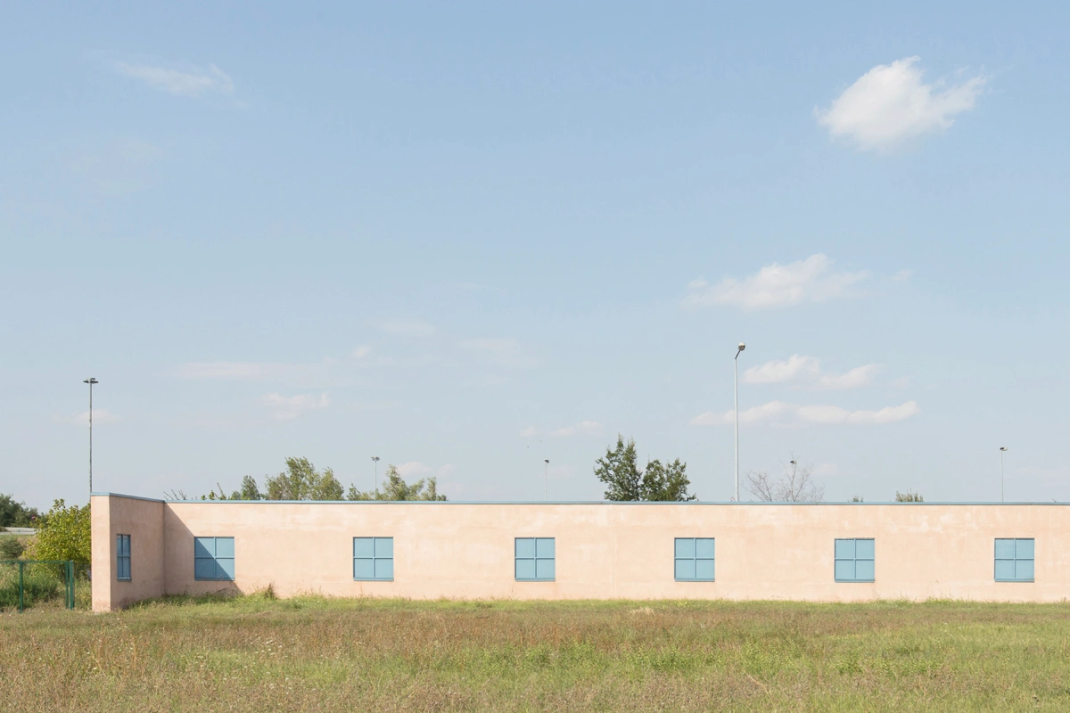 San Cataldo Cemetery by Aldo Rossi — A single-story institutional building with a peach-rendered facade extends horizontally across flat agricultural land.