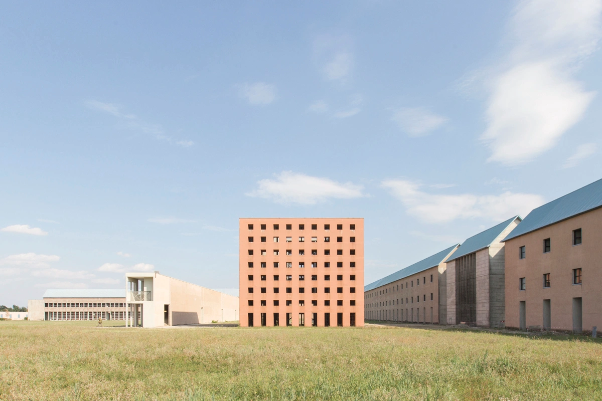 San Cataldo Cemetery by Aldo Rossi — Aldo Rossi's San Cataldo Cemetery presents a composition of three distinct brick structures across an open field under clear sky.