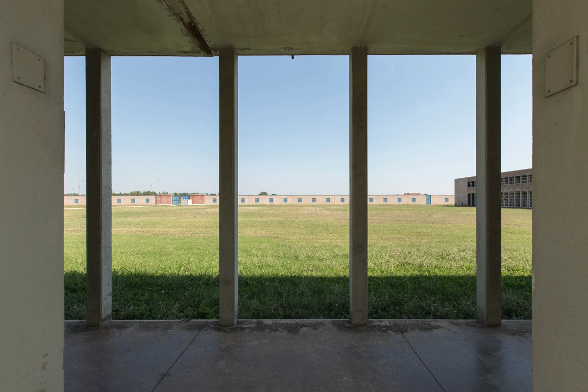 San Cataldo Cemetery by Aldo Rossi — Viewed from a sheltered portico, the photograph frames the San Cataldo Cemetery's expansive landscape through a colonnade of concrete pillars.