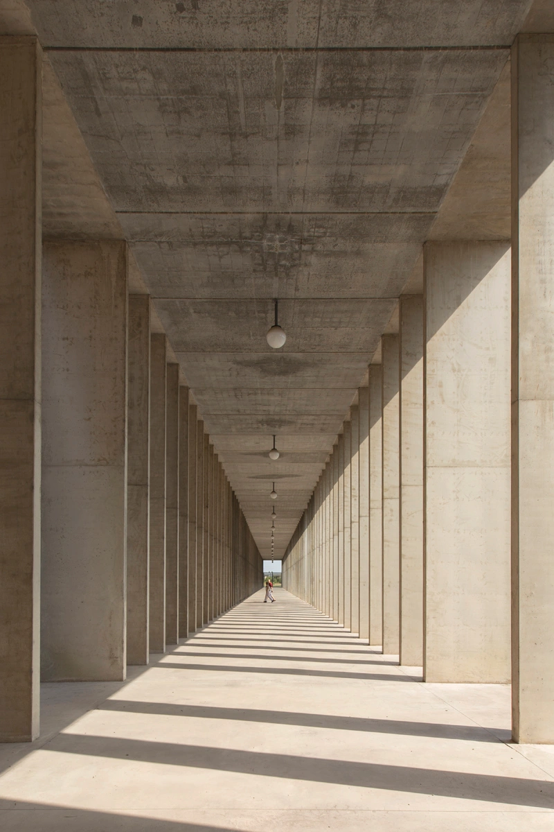 San Cataldo Cemetery by Aldo Rossi — A receding colonnade of concrete pillars frames a vanishing-point perspective toward distant daylight.
