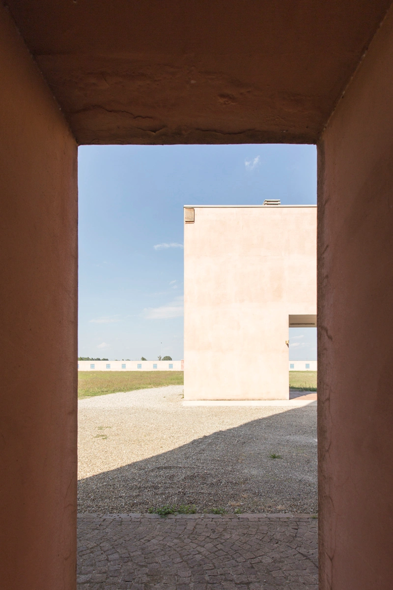 San Cataldo Cemetery by Aldo Rossi — Framed through a deep terracotta brick passage, the photograph captures a sectional view of San Cataldo Cemetery's volumetric cubic form.