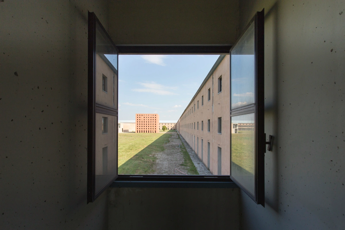 San Cataldo Cemetery by Aldo Rossi — Photograph taken from within a concrete-walled corridor, framing the view through an open double-leaf window with black metal frame.