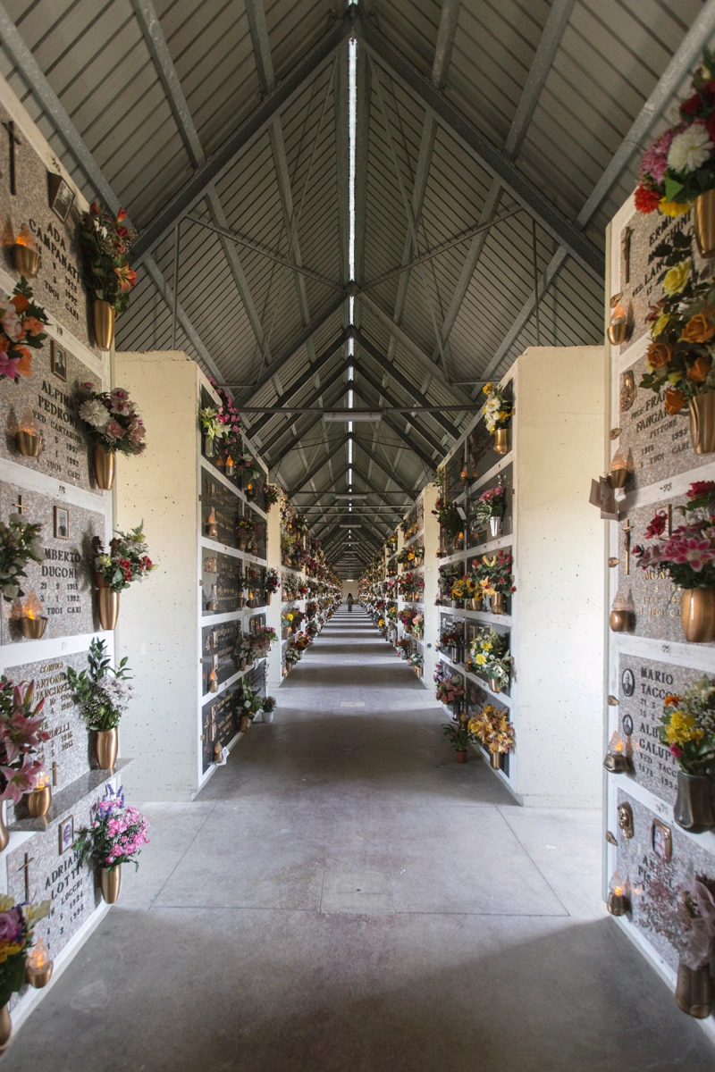 San Cataldo Cemetery by Aldo Rossi — A perspectival corridor stretches through San Cataldo Cemetery's columbarium, lined with terracotta brick walls punctuated by bronze vases and potted flowers.