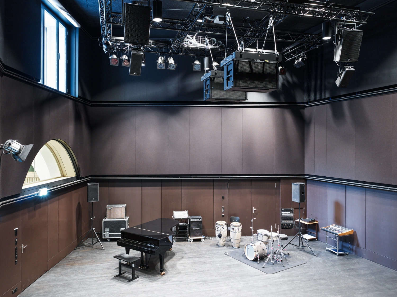 Jazz Campus by Buol & Zünd — A performance studio centered on a grand piano positioned beneath a complex overhead installation of suspended timber and metal framework.