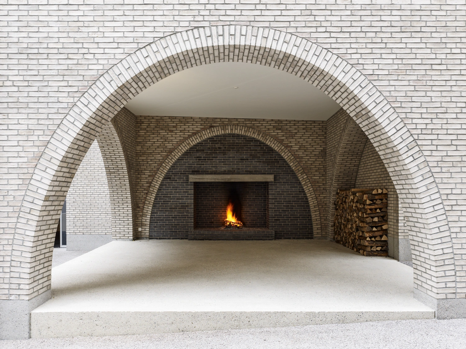 Jazz Campus by Buol & Zünd — A vaulted brick passage frames a deeper interior chamber where a fireplace glows with active flame.