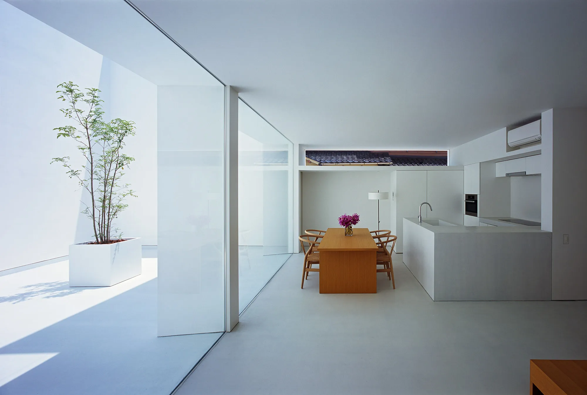 White Cave House by Takuro Yamamoto — The dining area occupies a central position within the White Cave House's open-plan interior, a wooden table with mid-century chairs anchoring the space...