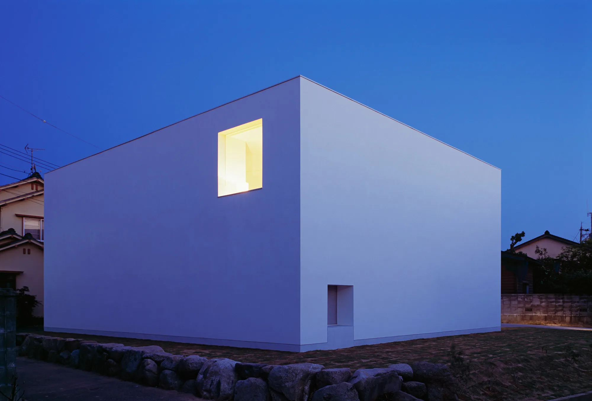 White Cave House by Takuro Yamamoto — White Cave House presents a monolithic rendered facade in pure white, punctuated by a single illuminated window on the upper level and a recessed void at...