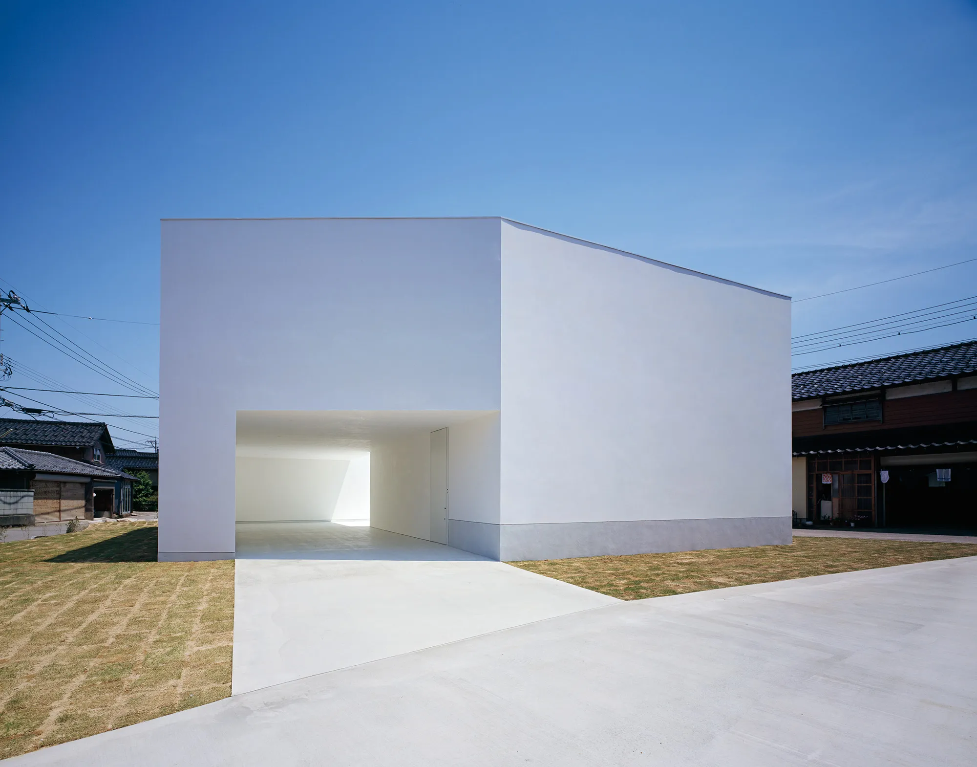 White Cave House by Takuro Yamamoto — White Cave House presents a monolithic rendered facade punctuated by a deep recessed void that functions simultaneously as carport and entry passage.