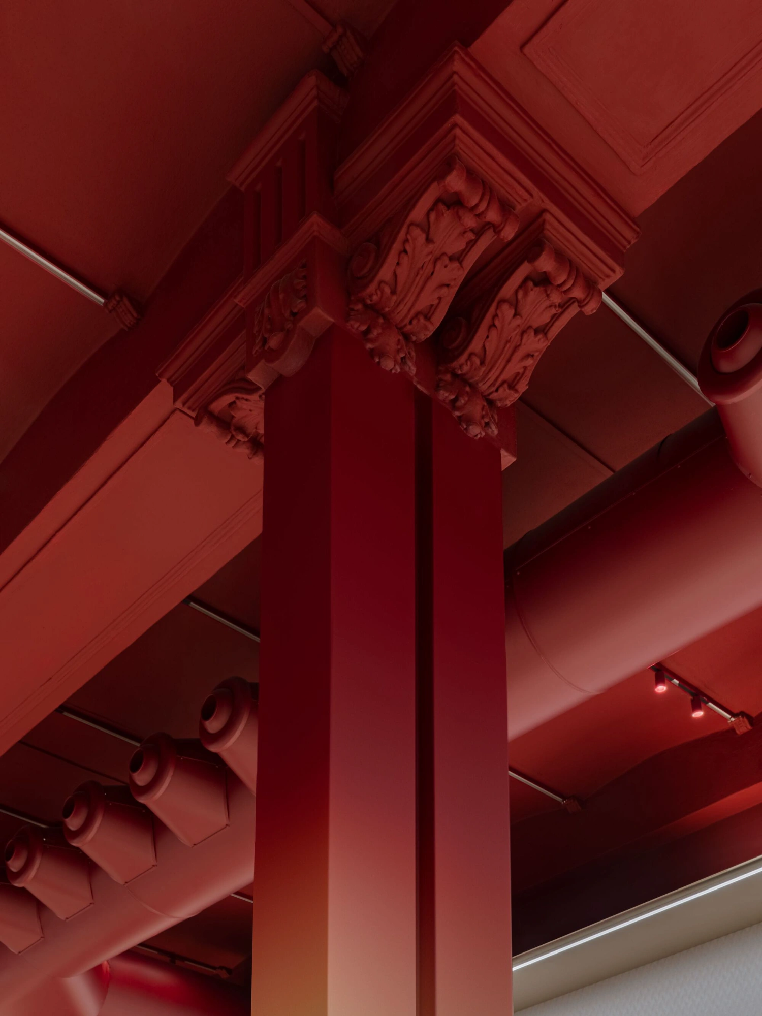 Missoni Home Boutique (Showroom) by Lit Studio — Overhead view of the showroom's structural centerpiece: three tapered columns in neutral tone rise through a deep crimson coffered ceiling articulated with...