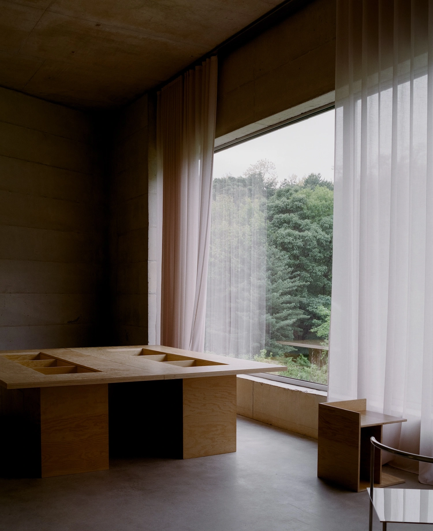 Raw House by Order Matter — A kitchen counter in raw timber occupies the foreground, its surface punctuated by geometric cutouts and a recessed sink.