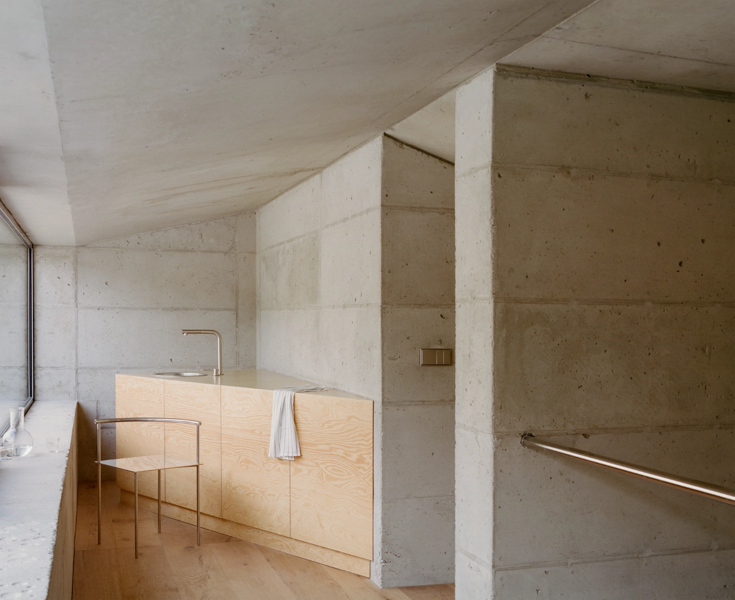 Raw House by Order Matter — A narrow passage compressed between monolithic concrete structural columns frames the domestic interior of Raw House.