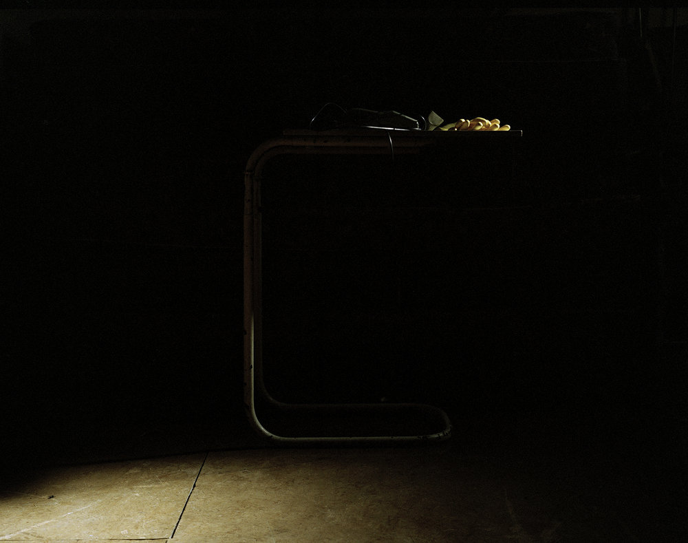After Magdalene by Ethna Rose O'Regan — A cast-iron pipe fixture dominates the composition, its weathered surface rendered in deep charcoal against absolute black.