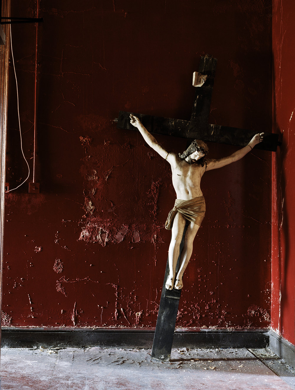After Magdalene by Ethna Rose O'Regan — A crucifix sculpture mounted on a weathered burgundy wall within the disused Magdalene Laundry.