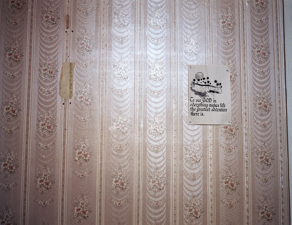 After Magdalene by Ethna Rose O'Regan — A domestic interior wall papered in floral damask pattern, mauve and cream tones arranged in vertical stripes with repeating botanical motifs.
