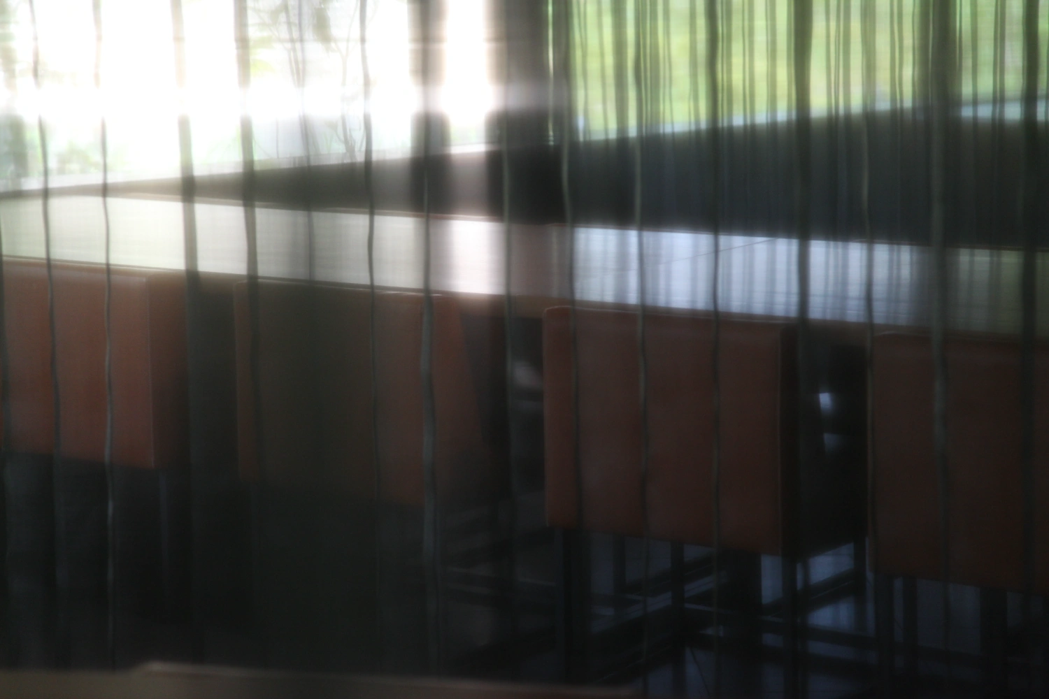 Sayama Lakeside Cemetery Community Hall by Hiroshi Nakamura & NAP — Interior view through a metal-framed gridded partition, looking toward glazed fenestration framing forest canopy.