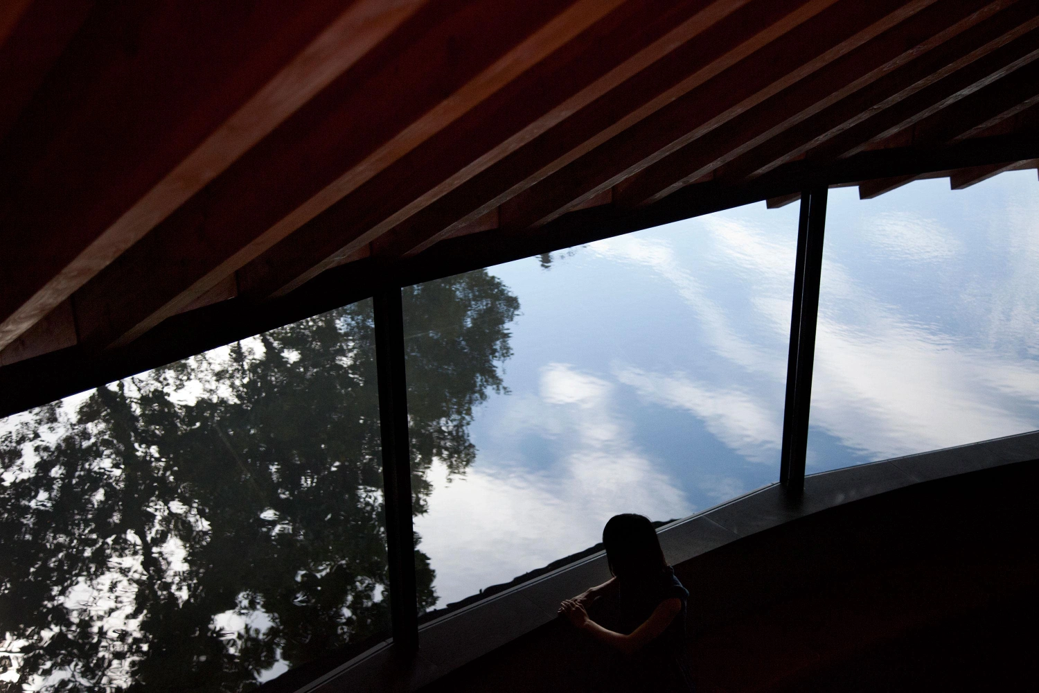 Sayama Lakeside Cemetery Community Hall by Hiroshi Nakamura & NAP — From within the hall, the steeply pitched timber roof beams create a rhythmic linear pattern across the ceiling, their diagonal geometry directing sight upward.