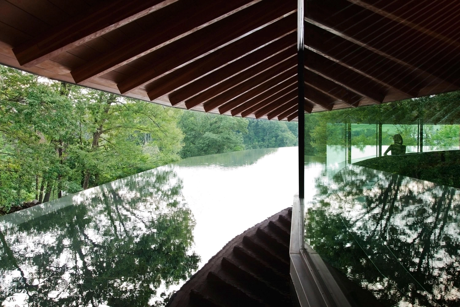 Sayama Lakeside Cemetery Community Hall by Hiroshi Nakamura & NAP — The viewing platform extends into the landscape through floor-to-ceiling glazing, positioning the seated occupant at eye level with the reflected forest...