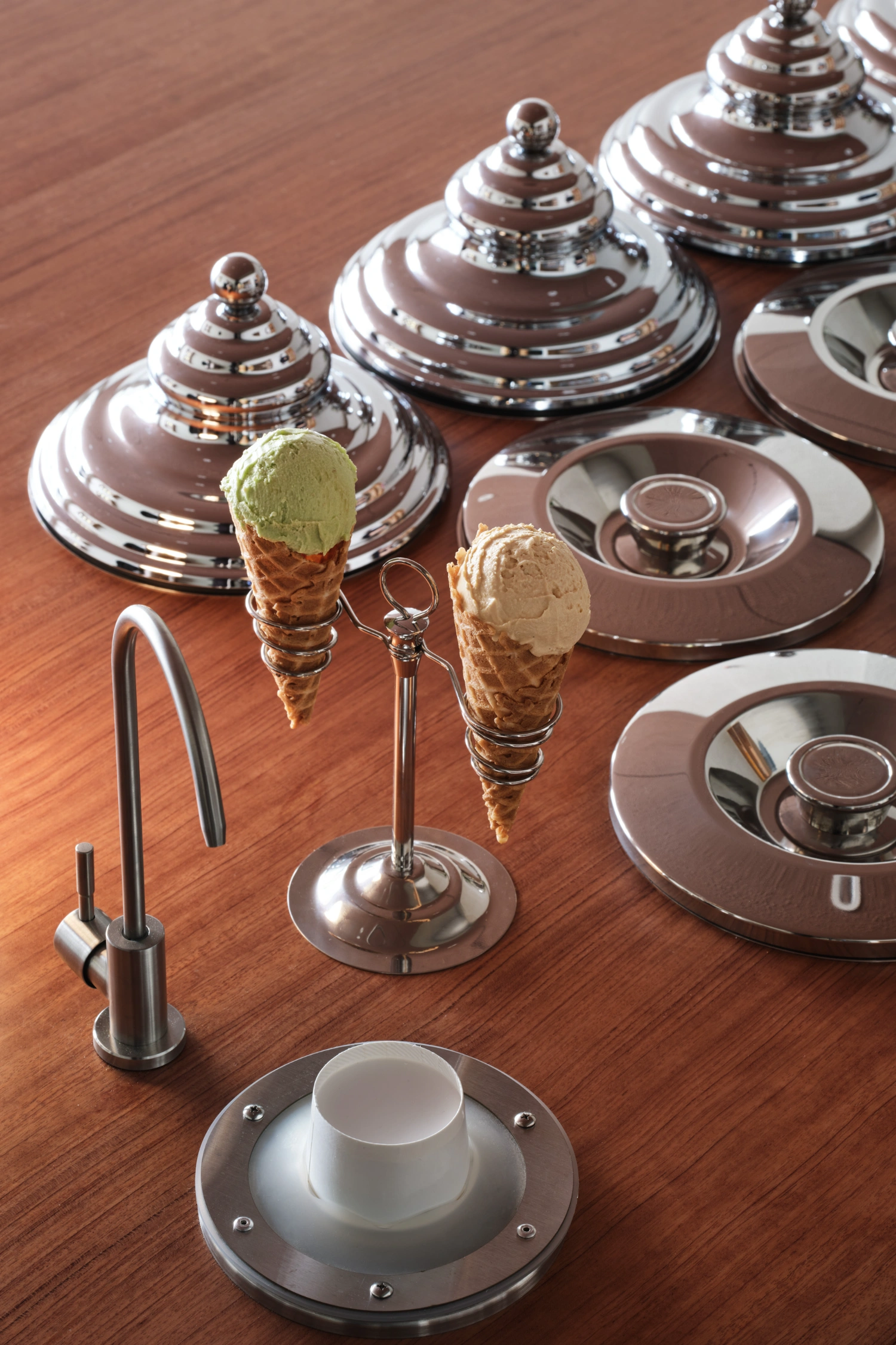 PINOCCHIO Gelato + Coffee Shop by WARP AND WOOF — Detail shot of the gelato shop's service counter, staging ice cream cones in pistachio green and vanilla within chrome-plated holders.