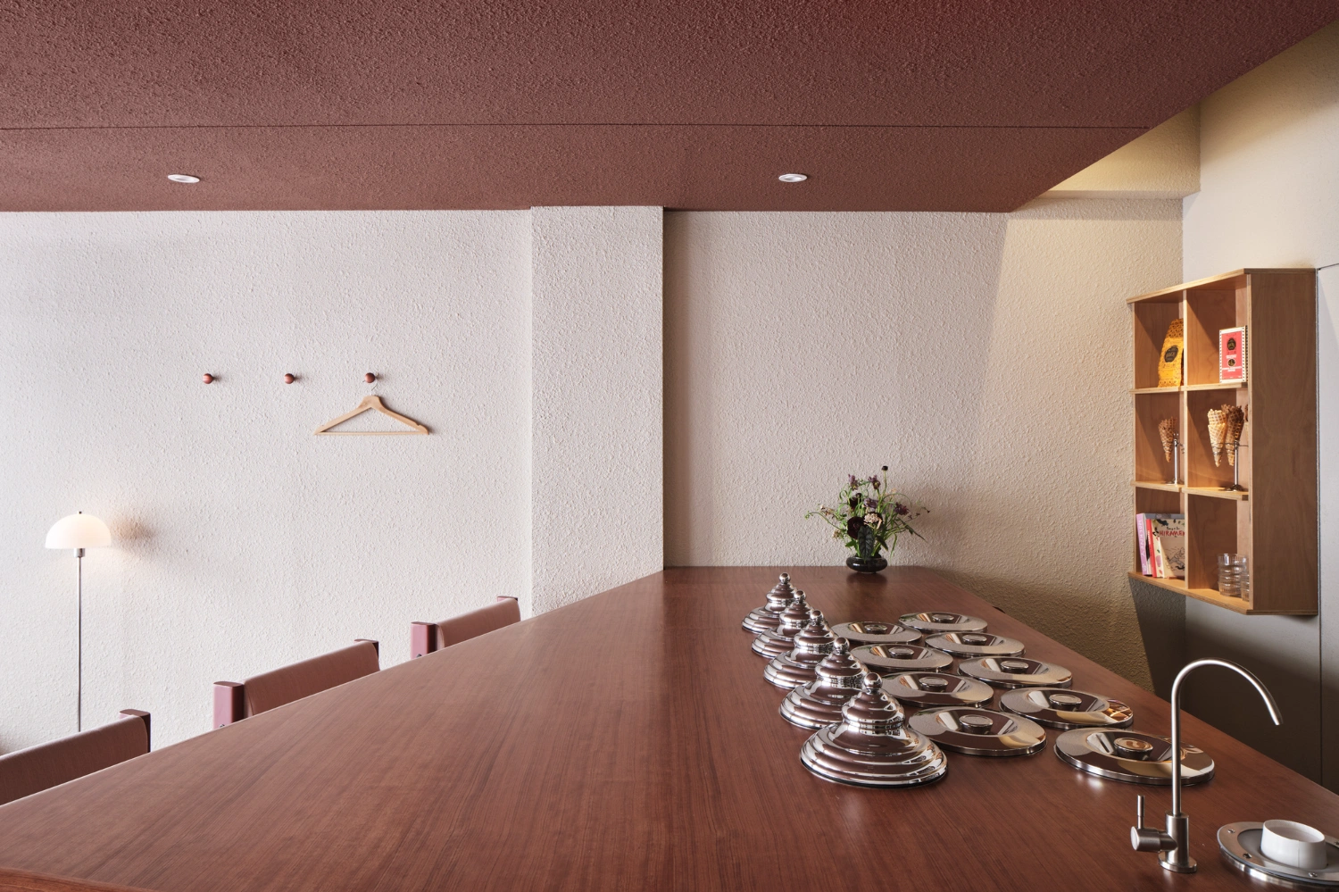 PINOCCHIO Gelato + Coffee Shop by WARP AND WOOF — The dining table occupies the center of this narrow gelato shop interior, lined with small silver serving vessels and matching plates arranged in precise rows.