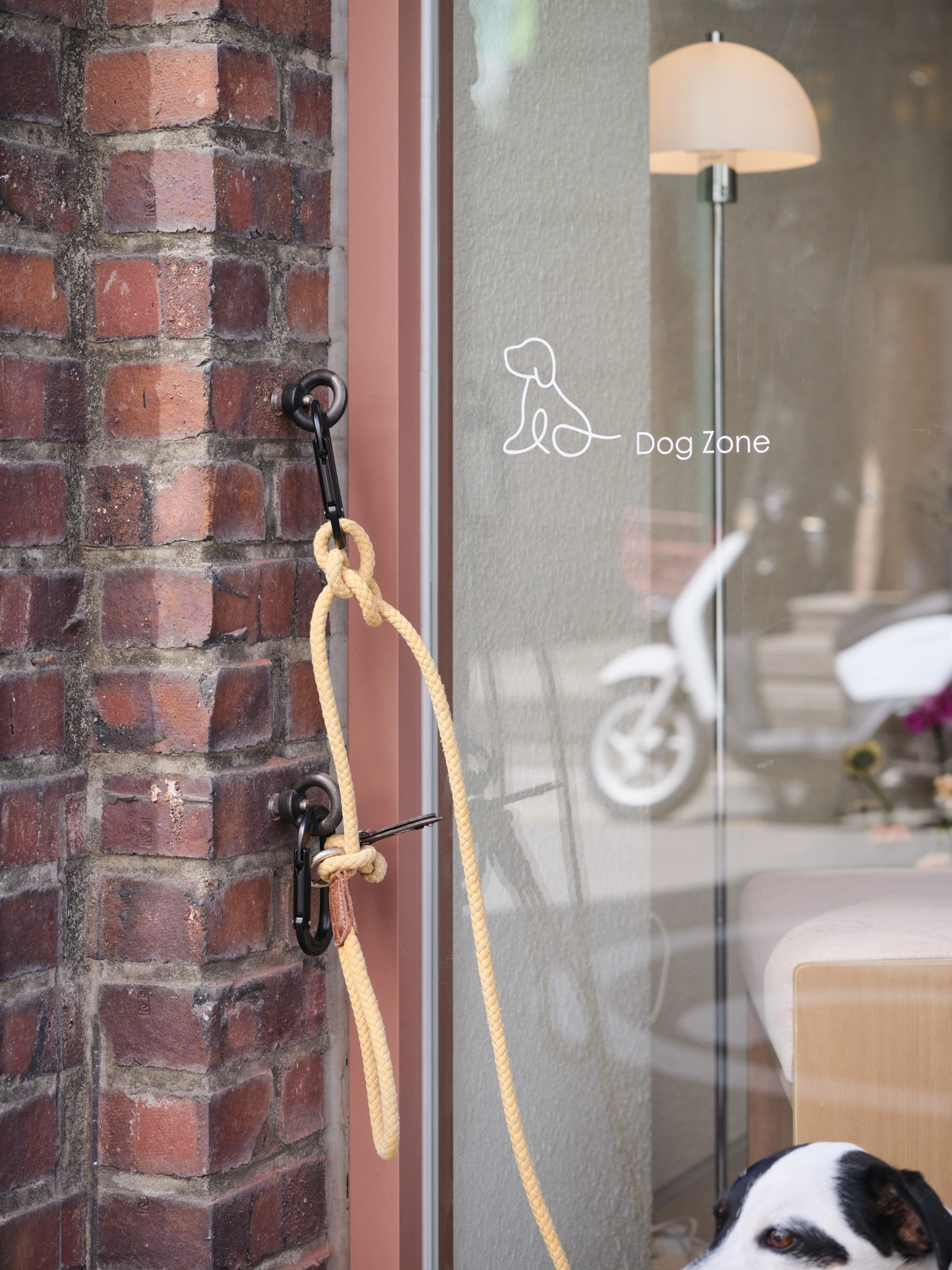 PINOCCHIO Gelato + Coffee Shop by WARP AND WOOF — A rope leash hangs from black metal hooks mounted on a weathered brick facade, terminating in a simple knot.
