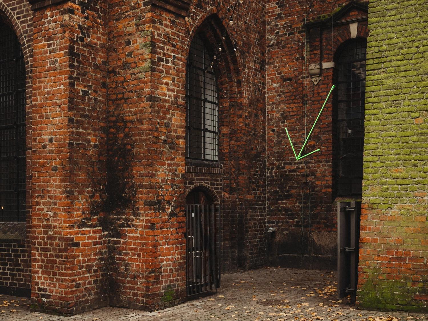 Nikolaj Kunsthal Café + Boutique by Engel Architects by MEE Studio — Exterior courtyard framed by weathered brick masonry with moss-covered stone on the right wall.