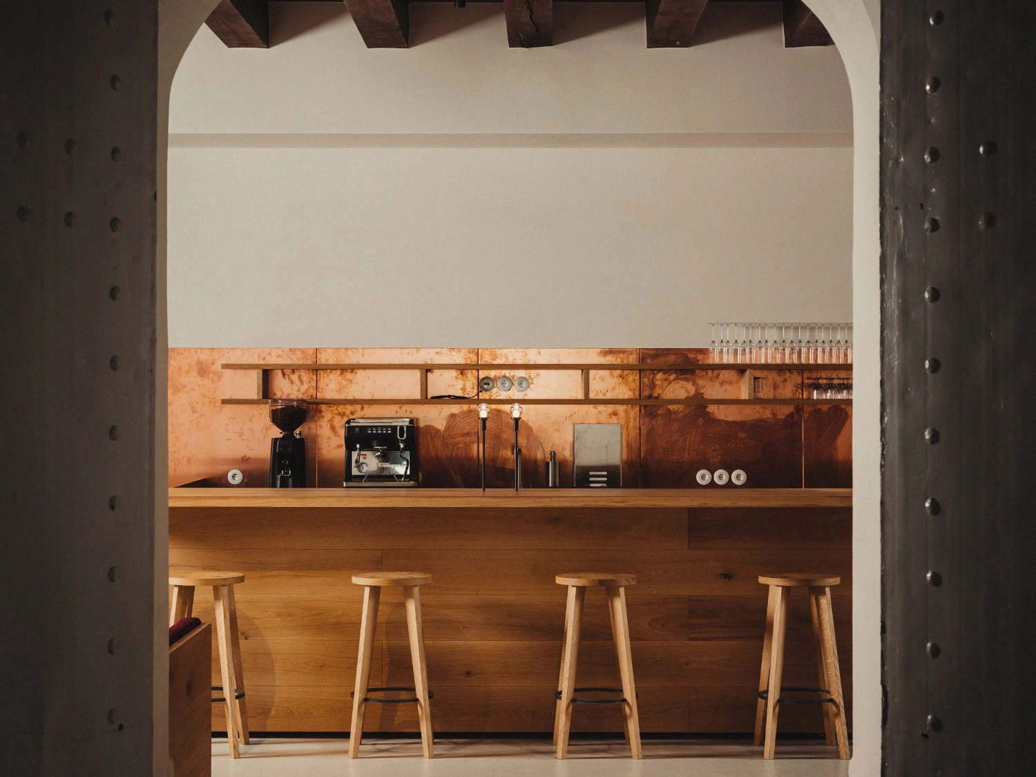 Nikolaj Kunsthal Café + Boutique by Engel Architects by MEE Studio — A café counter viewed through a rounded archway framed by perforated metal panels.