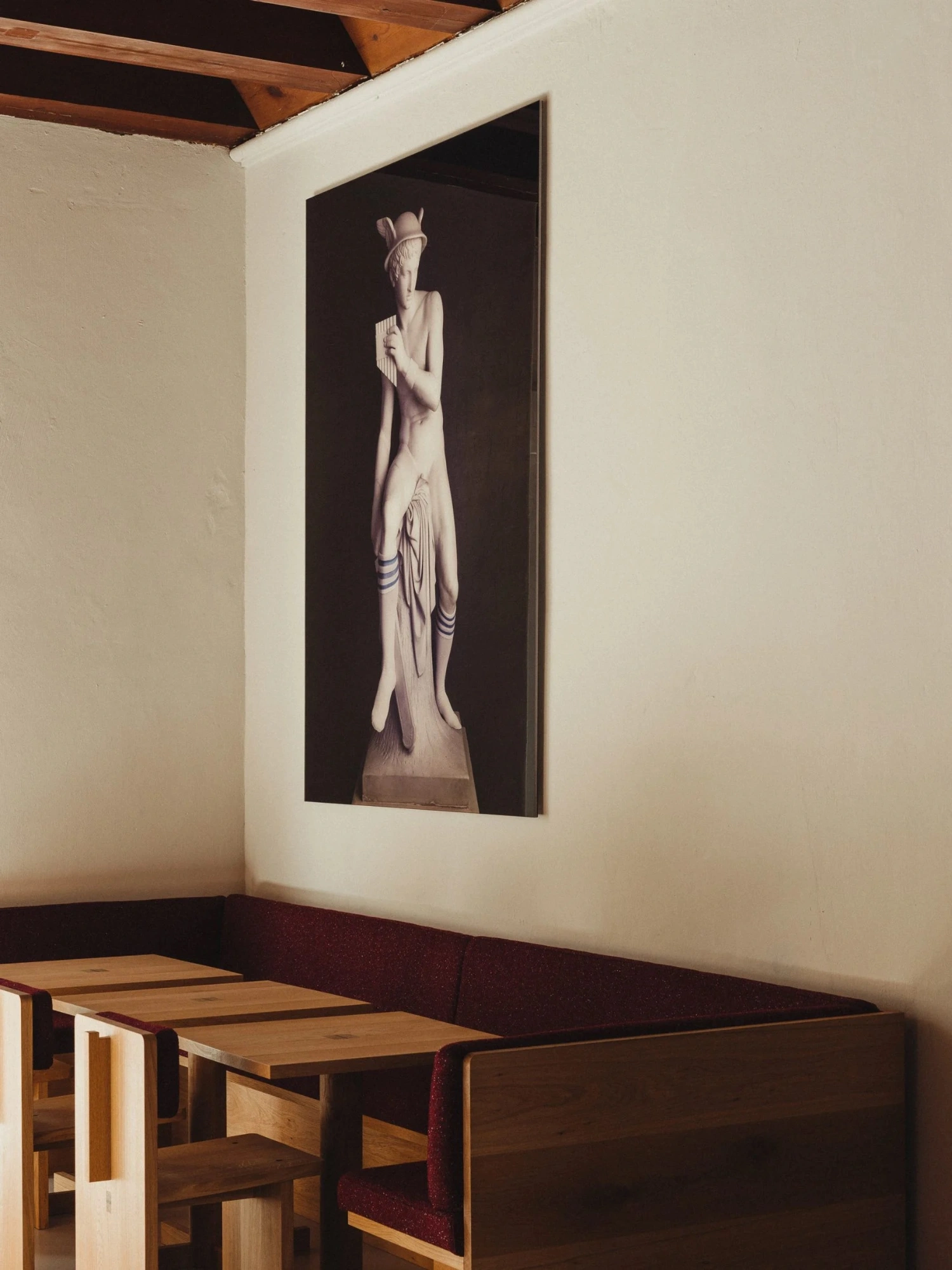 Nikolaj Kunsthal Café + Boutique by Engel Architects by MEE Studio — A vertical sculptural photograph commands the cream plaster wall above wooden furniture.
